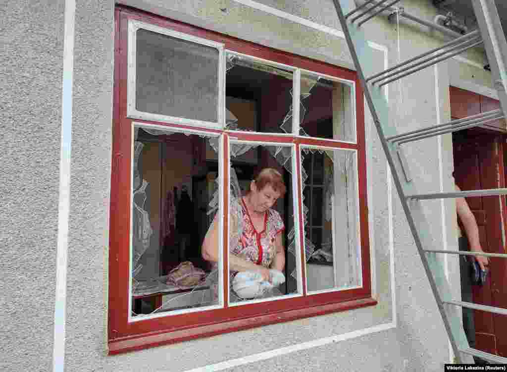 A woman clears shards of glass from a shattered window that was damaged during the attack in Mykolayiv. &nbsp;