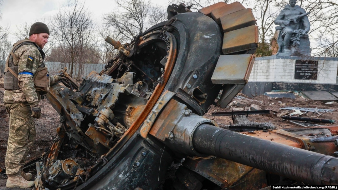 Український військовослужбовець оглядає залишки знищеного російського танка у нещодавно звільненому селі Лук'янівка Київської області, 27 березня 2022 року