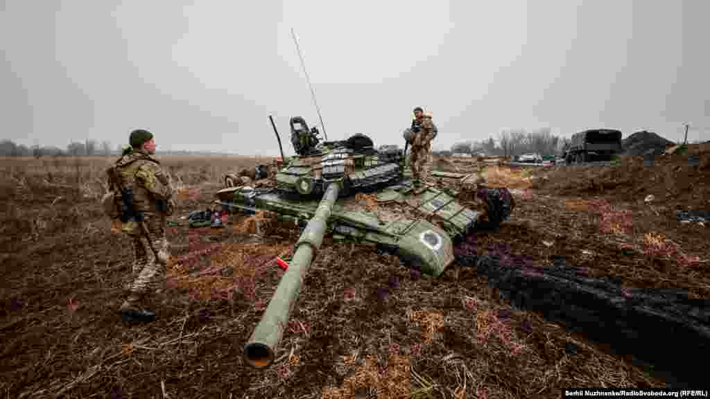 Украинские военные осматривают застрявший в грязи российский танк