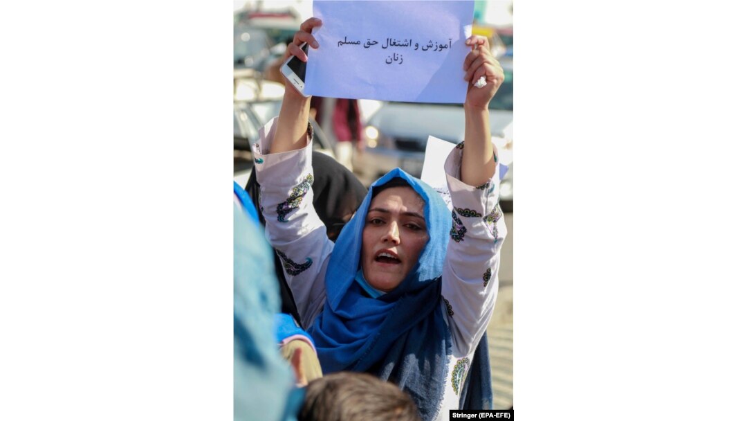 An Afghan woman holds a sign saying, "Education and employment are the inalienable rights of Muslim women."