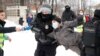Un bărbat care poartă o vestă de presă întinde un microfon în timp ce poliția reține un protestatar în timpul unui miting împotriva arestării lui Alexei Navalnîi