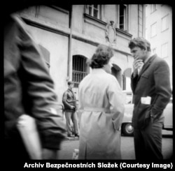 Čehoslovački autor Milan Kundera (desno) razgovara sa saradnikom. Knjiga iz 2008. godine pod nazivom Prag kroz objektiv tajne policije, iz koje su izvedene mnoge ove slike, identifikuje muškarca u kožnoj košulji u pozadini kao agenta koji upravlja kamerom skrivenom u koferu. Špijunske kamere mogle su se pokrenuti tankim kabelom, omogućavajući fotografisanje bez dodirivanja samog uređaja.