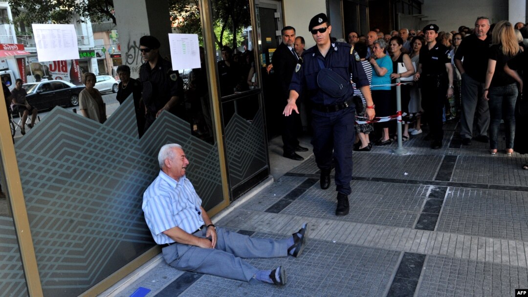 A man sits on the sidewalk crying outside a national bank branch as pensioners queue to withdraw their pensions, with a limit of 120 euros, in Thessaloniki.