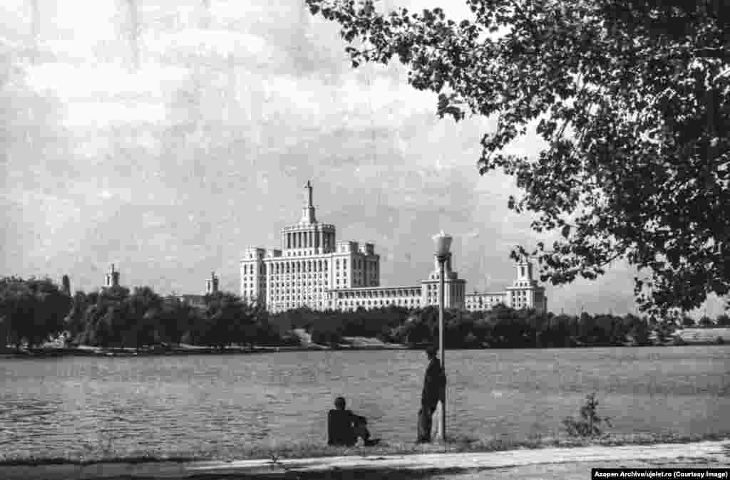 Doi bărbați privesc peste Lacul Herăstrău din București spre Casa Scânteii, o clădire construită după modelul Universității Lomonosov de la Moscova, și care a găzduit cele mai multe dintre ziarele comuniste de stat din România lui Ceaușescu. Szocs este unul dintre fondatorii Azopan, o arhivă fotografică cu acces liber care conține în mare parte fotografii făcute de amatori din secolul al XX-lea din România, ceea ce înseamnă că infrastructura necesară pentru a crea arhiva Uj Elet era deja în mare parte existentă. 