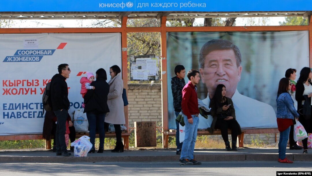 People wait for a bus in front of election campaign posters at a bus stop in the Kyrgyz capital, Bishkek. The country goes to the polls to elect a new president on October 15. 